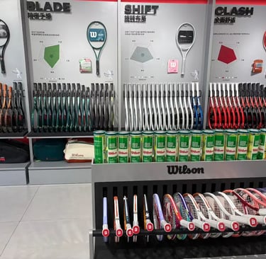 A retail display of Wilson tennis rackets including Blade, Clash, and Shift models with tennis ball cans.