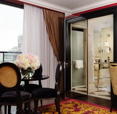 Luxury hotel suite interior featuring elegant furniture, a dining area, and a view of the city skyline.