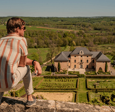 A man overlooking a historic French chateau and manicured gardens in the countryside.