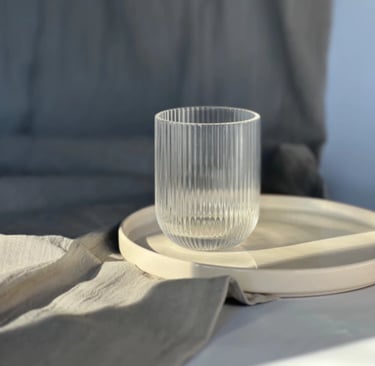 Elegant ribbed glass tumbler sitting on a white ceramic tray with soft linen textures.