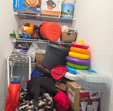 Cluttered laundry closet with shelves holding boxes, toys, and tools above a messy washing machine.