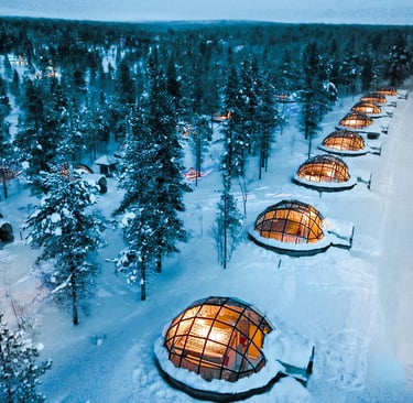 Luxury glass igloos illuminated at night in a snowy Lapland pine forest for winter tourism.