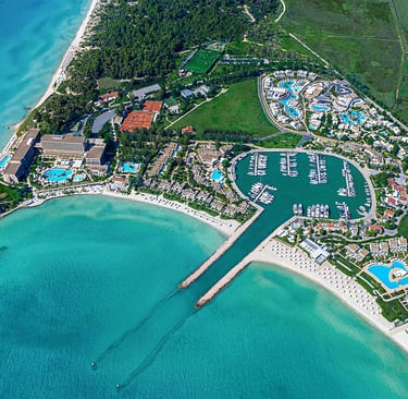 Aerial view of  Sani Resort Halkidiki, Greece with a private yacht marina and turquoise ocean water.