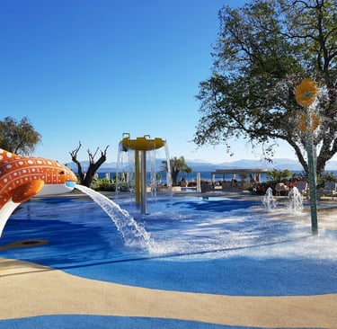 Outdoor kids splash pad with a whale fountain and water spray features at a sunny luxury resort.