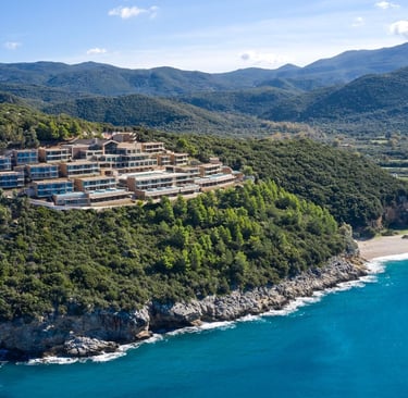 Luxury hillside resort overlooking the turquoise Ionian Sea and lush green mountains in Greece.