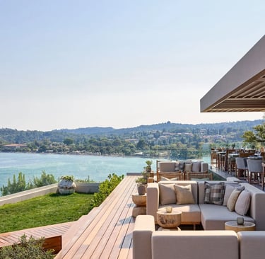 Ikos Odisia lounge and restaurant terrace overlooking a blue ocean bay and lush coastline.