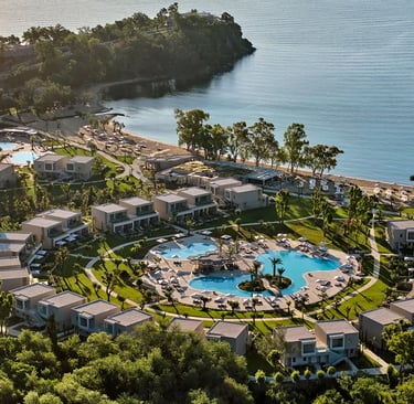 Aerial view of a luxury beachfront resort with circular pools, modern villas, and a private bay.