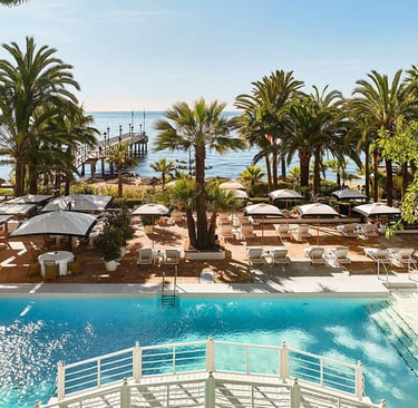 Luxury beach resort with an outdoor swimming pool, palm trees, and ocean views featuring a wooden pier.