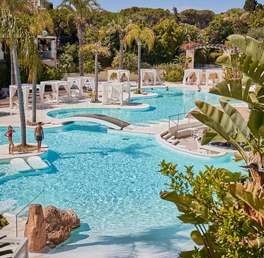Luxury tropical resort swimming pool with white cabanas, palm trees, and turquoise water.