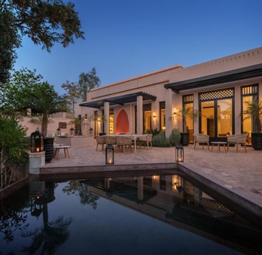 Luxury villa patio with a dark swimming pool, outdoor dining set, and lanterns at twilight.