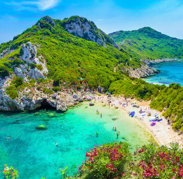 Panoramic view of  Rovinia beach in Corfu, Greece, with turquoise waters and lush green cliffs.