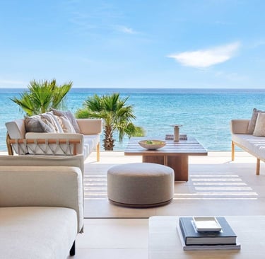 Luxury outdoor patio furniture on a balcony overlooking the turquoise ocean and palm trees.