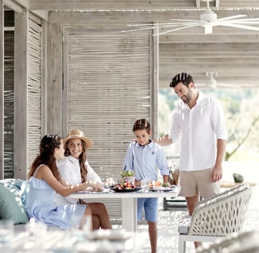A happy family enjoys a luxury outdoor brunch at Ikos Aria a sunlit beach resort patio.