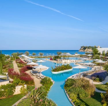 Luxury beachfront resort featuring a sparkling blue infinity pool, white sun umbrellas, and lush gardens overlooking the