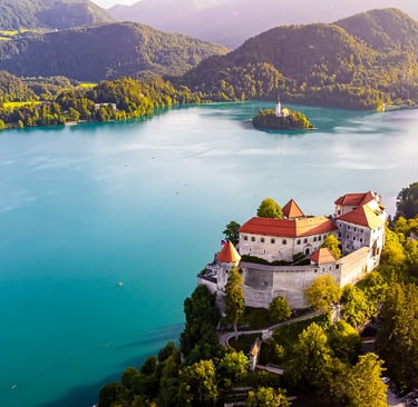 Aerial view of Bled Castle overlooking turquoise Lake Bled and the Pilgrimage Church of the Assumption in Slovenia.