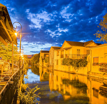Scenic night view of a canal in L'Isle-sur-la-Sorgue, France, with yellow buildings reflecting in the water.
