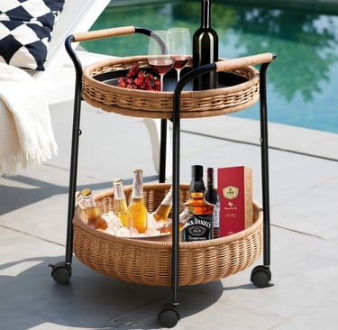 Two-tier wicker outdoor bar cart with wine and bottled drinks on a patio by a luxury swimming pool.