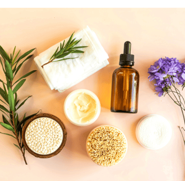 Natural skincare products including a serum dropper bottle, face cream, and body brush on a pink background.