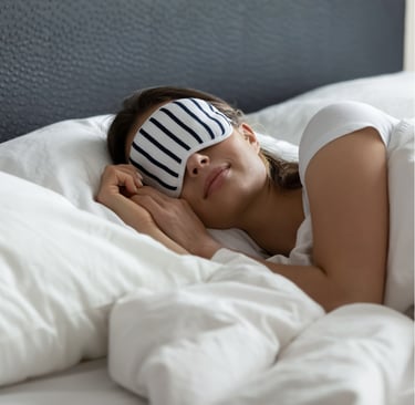 woman with sleeping mask on, sleeping happily in bed. goes with article about sleeping well everyday