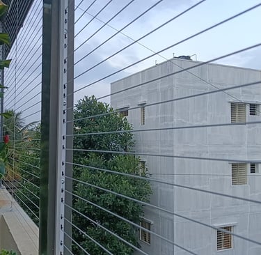 Side perspective of invisible grills installed on a high-rise apartment window overlooking greenery.