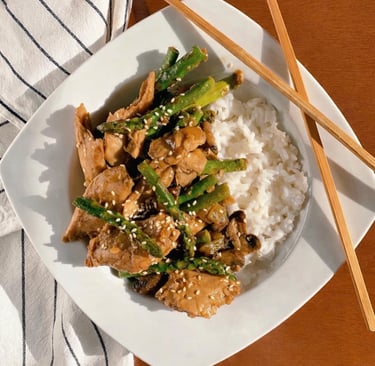Not Chicken and asparagus stir fry with sesame seeds served over white rice with chopsticks.