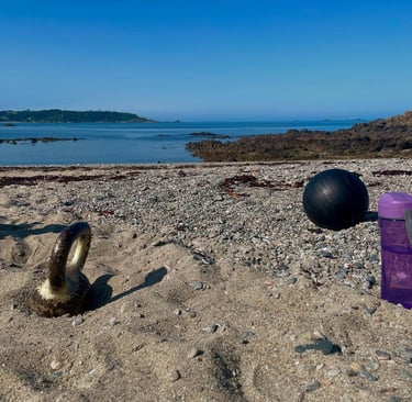 Fitness gear including a kettlebell, medicine ball, and water bottle for a beach workout.