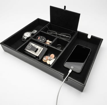 Black leather valet tray organizer for men holding a watch, wallet, coins, and charging smartphone.