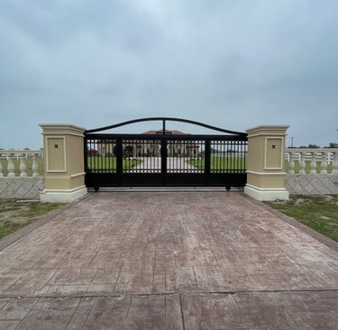 Automatic black wrought iron driveway gate with stone pillars leading to a luxury estate.