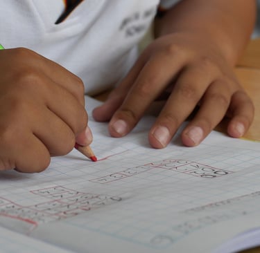 Two young, brown hands on paper, the right one writing with a colored pencil