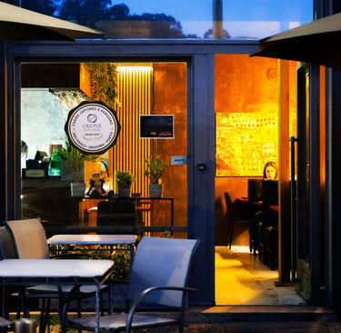Entrada do Okone Sushi no Porto com mesas externas, fachada de vidro e logótipo iluminado durante o entardecer.
