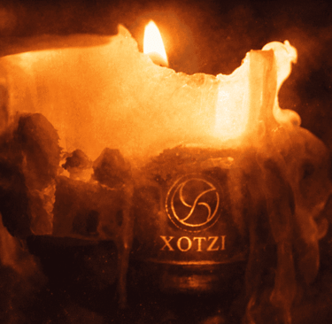 Una vela naranja brillante, con cera derritiéndose y una llama encendida, que presenta un logo xotzi