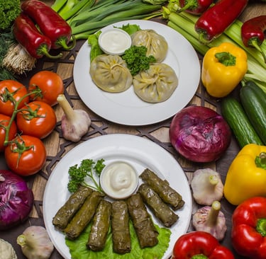 Two plates of fresh Mediterranean‑style dishes surrounded by colorful vegetables, including bell peppers, tomatoes 
