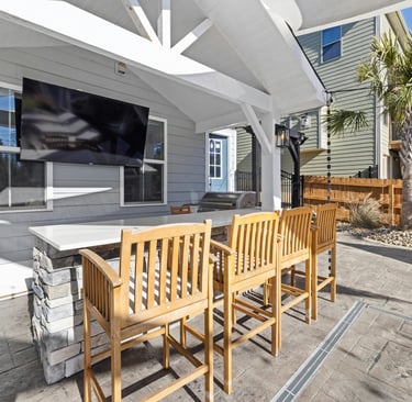 Covered outdoor bar area with wooden bar stools, a mounted TV, stone counter,