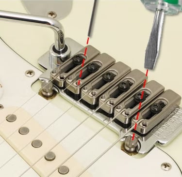 A person using a screwdriver to adjust the intonation on an electric guitar bridge system.