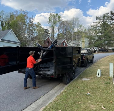 A worker loads a black dumps trailer on a residential street for junk removal services.