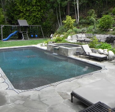 a pool with a raised spa and custom stone decking