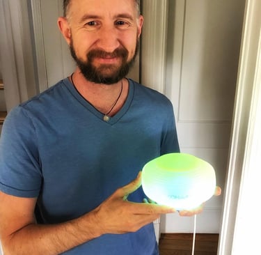 A man holding a glowing Somavedic device that emits a soft green and yellow light for EMF protection.