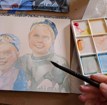 Artist painting a watercolor portrait of two young boys with a brush and mixing palette.