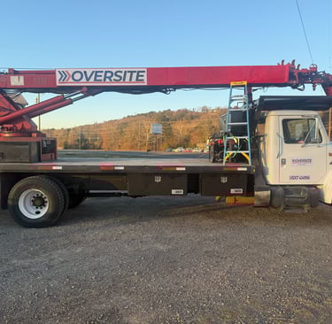 White Oversite boom truck with a red crane and flatbed parked in a gravel lot.