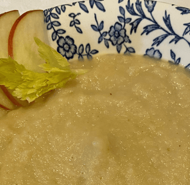 Creamy apple and celery root soup served in a blue floral patterned bowl with fresh garnishes.