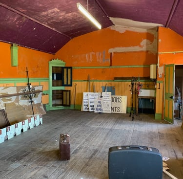 Old school hall with orange walls, storage units, and exposed structure pre-conversion.