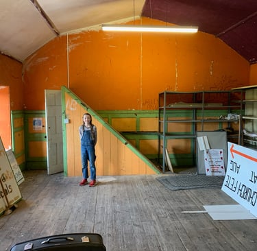 Renovation stage showing stripped hall with ladders, signs, and exposed surfaces.