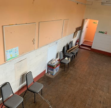 Empty classroom with noticeboards, stacked chairs, and exposed walls during early works.