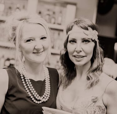 two girls dressed in 1920s costume are smiling at a themed murder mystery party.