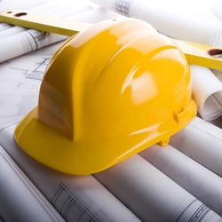 Yellow construction hard hat resting on architectural blueprints with a spirit level.