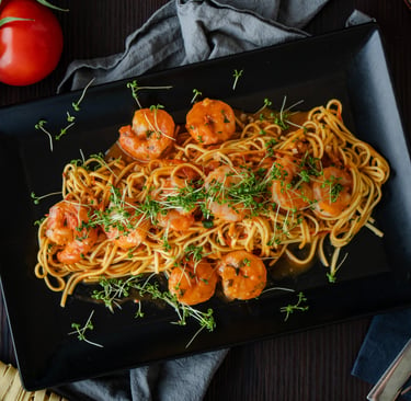 Spaghetti mit Garnelen in Tomatensauce und frischen Microgreens auf schwarzem Teller.