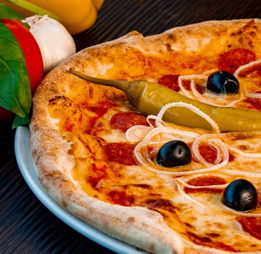 Heiße Pepperoni-Pizza mit schwarzen Oliven, Zwiebeln und grünen Paprika neben frischen Basilikumblät
