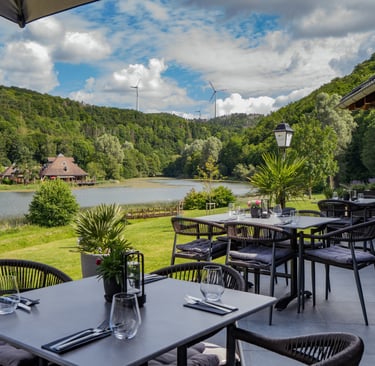 Outdoor-Seeterrasse mit moderner Möblierung und Blick auf ein Tal mit Windrädern.