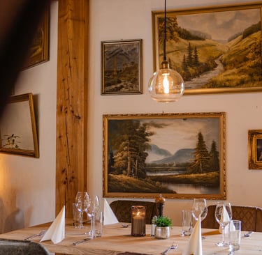 Elegant gedeckte Restauranttische mit edlem Glasgeschirr und Landschaftsgemälden an der Wand.