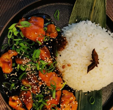 Bourbon Chicken mit Sesam und Frühlingszwiebeln auf Reis, dunkel fotografiert